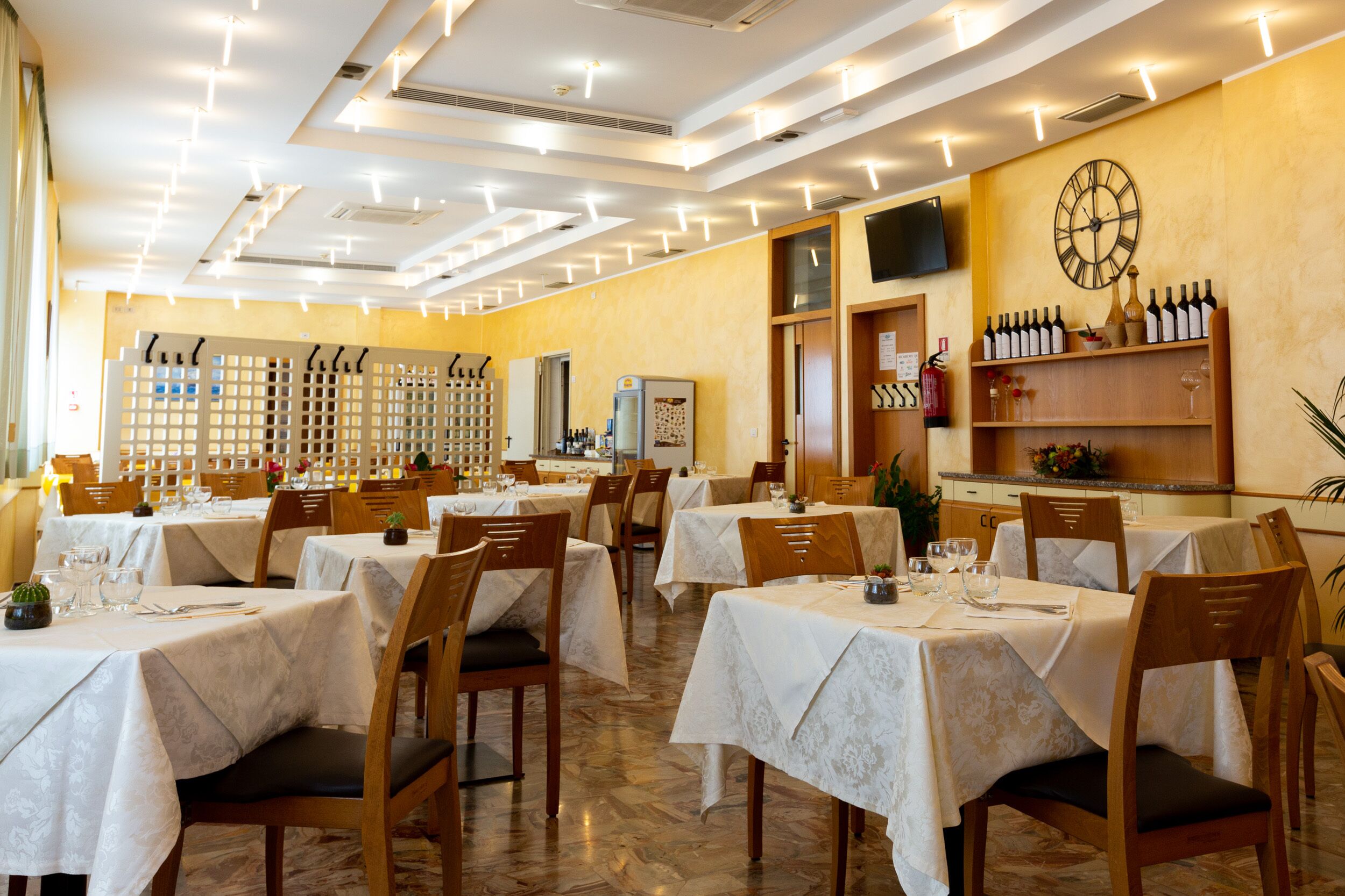 Ein Restaurant mit mehreren Tischen, Stühlen, einer Uhr und einer Weinauslage.