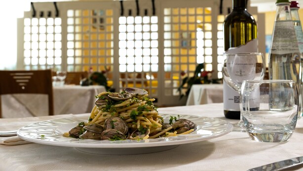 Una mesa de comedor con un plato de pasta, una botella de vino y un vaso de agua.