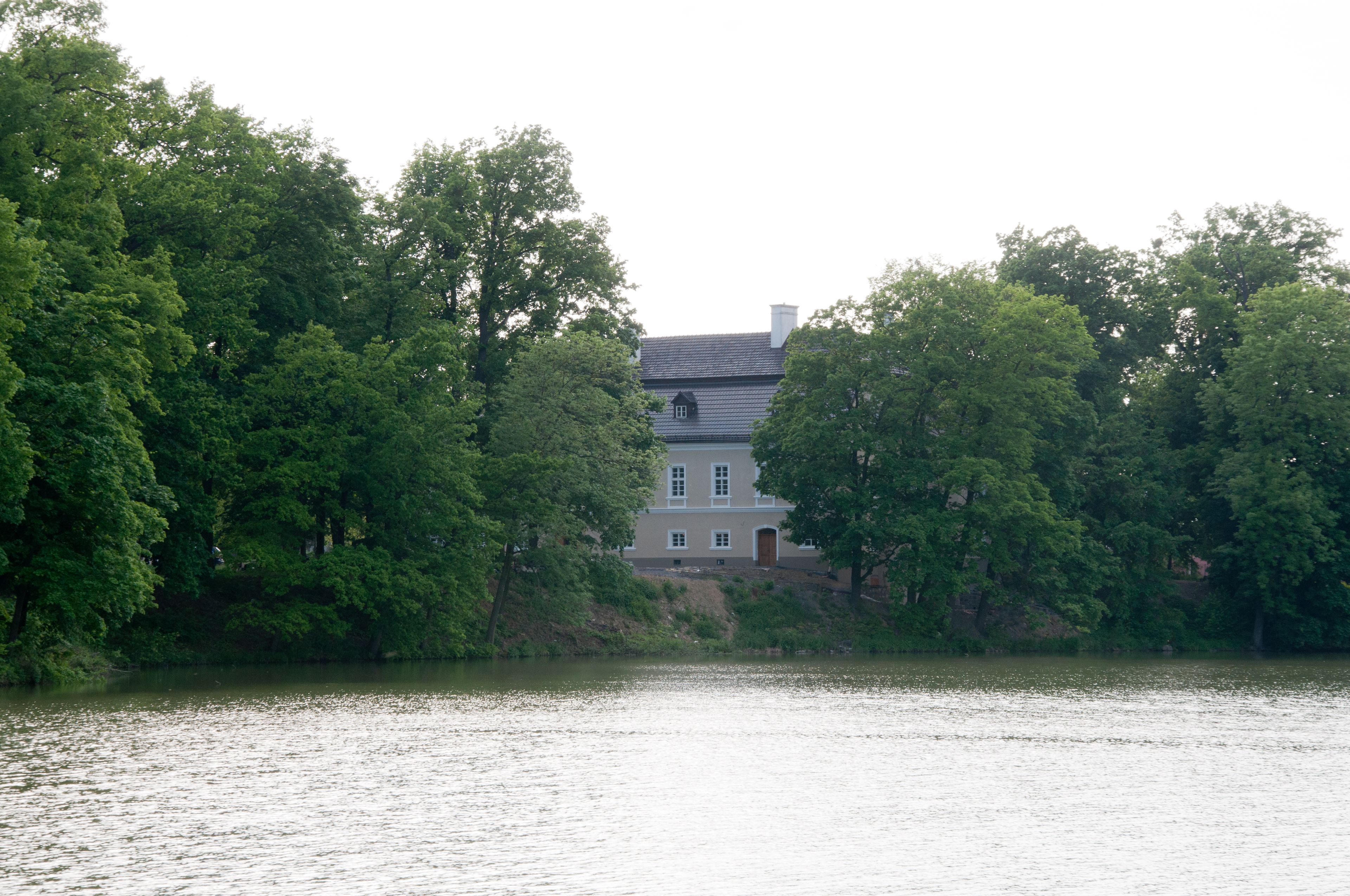 Una casa junto a un lago, con árboles densos a ambos lados.