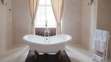 Un baño con una bañera independiente, cortinas color beige, un ventanal con vistas y un perchero para toallas.