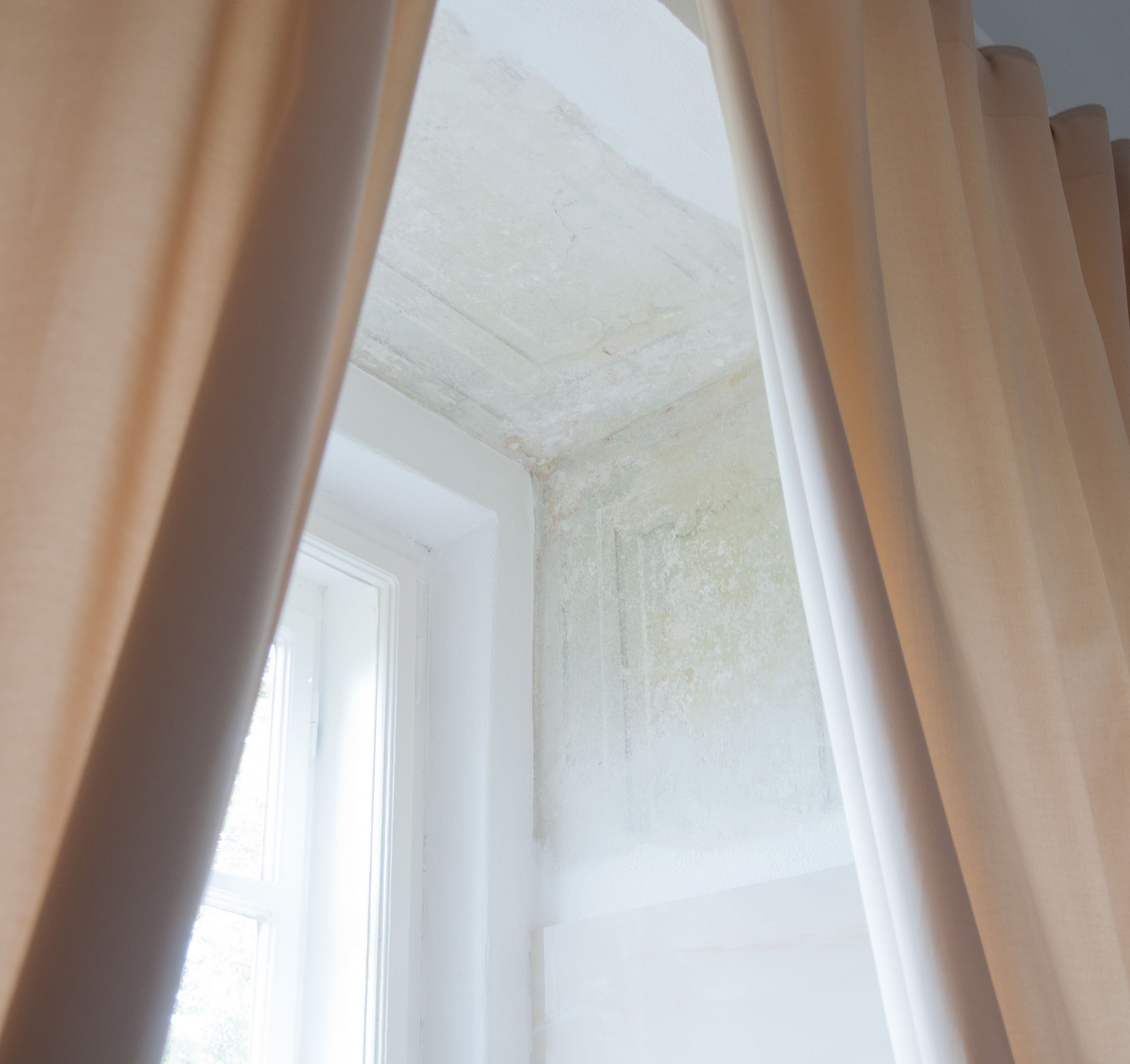 A room corner with a white ceiling and walls, a window, and curtains.