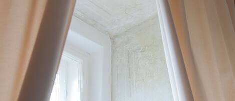 A room corner with a white ceiling and walls, a window, and curtains.