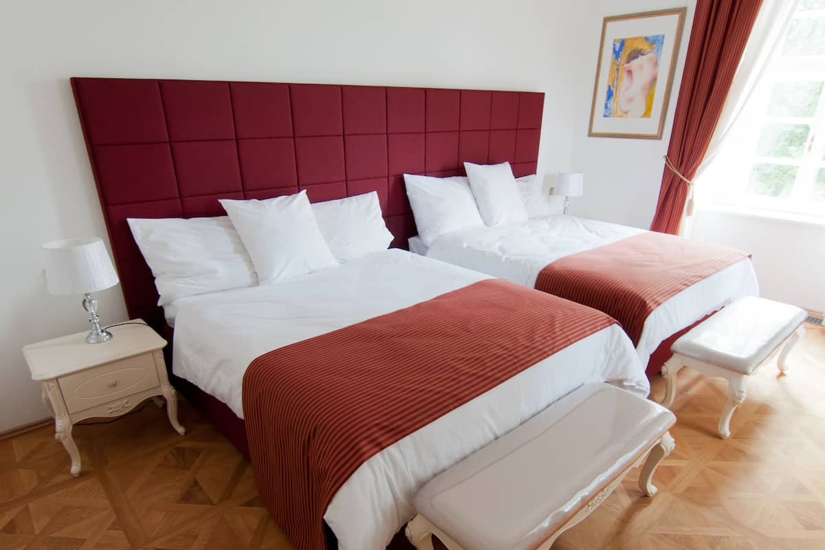 Ein Hotelzimmer mit zwei Betten, einem Nachttisch, einer Bank und einem Fenster mit Vorhängen.