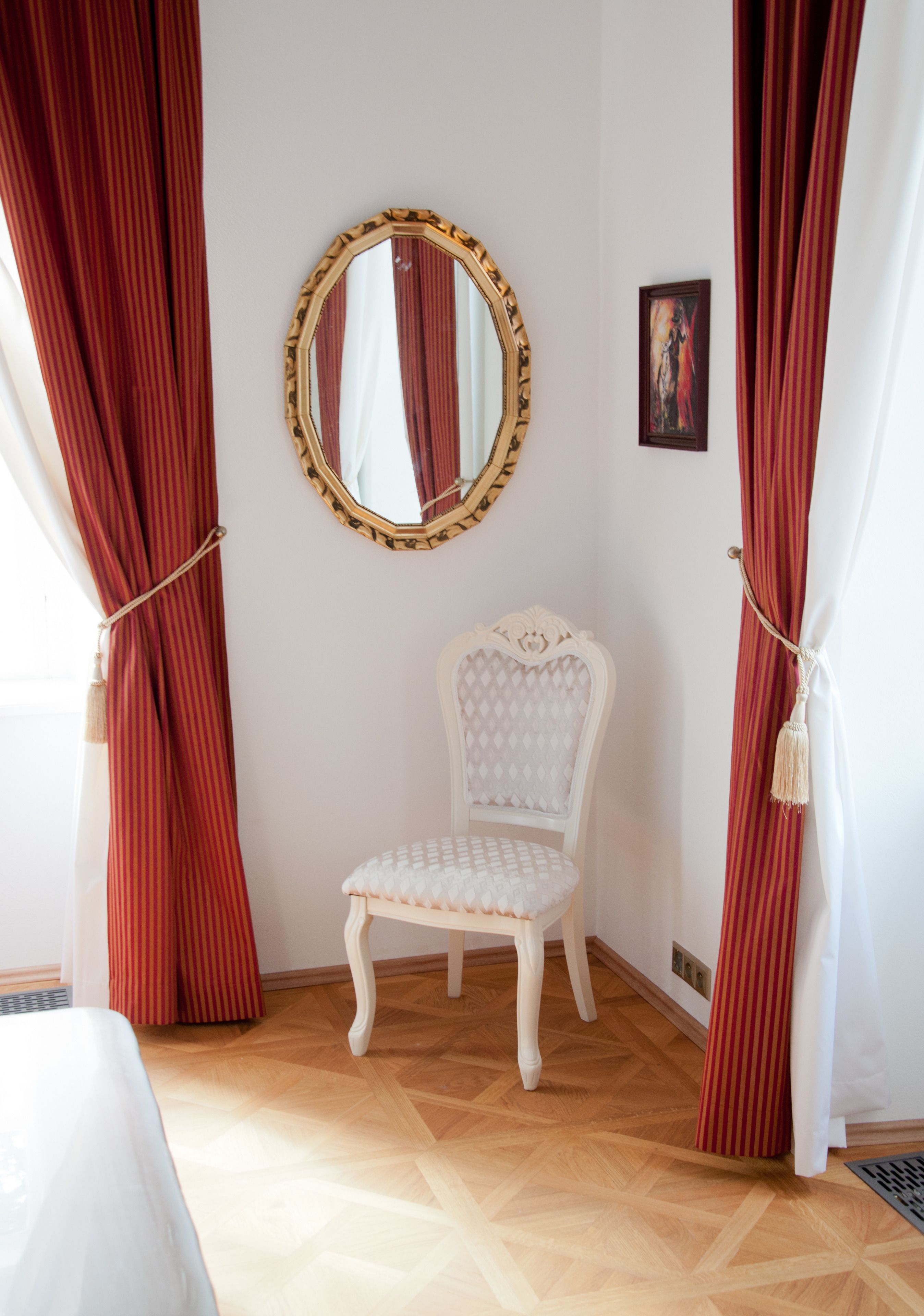 Une pièce avec un fauteuil recouvert de tissu blanc, un miroir rond doté d’un cadre doré et des rideaux rouges.