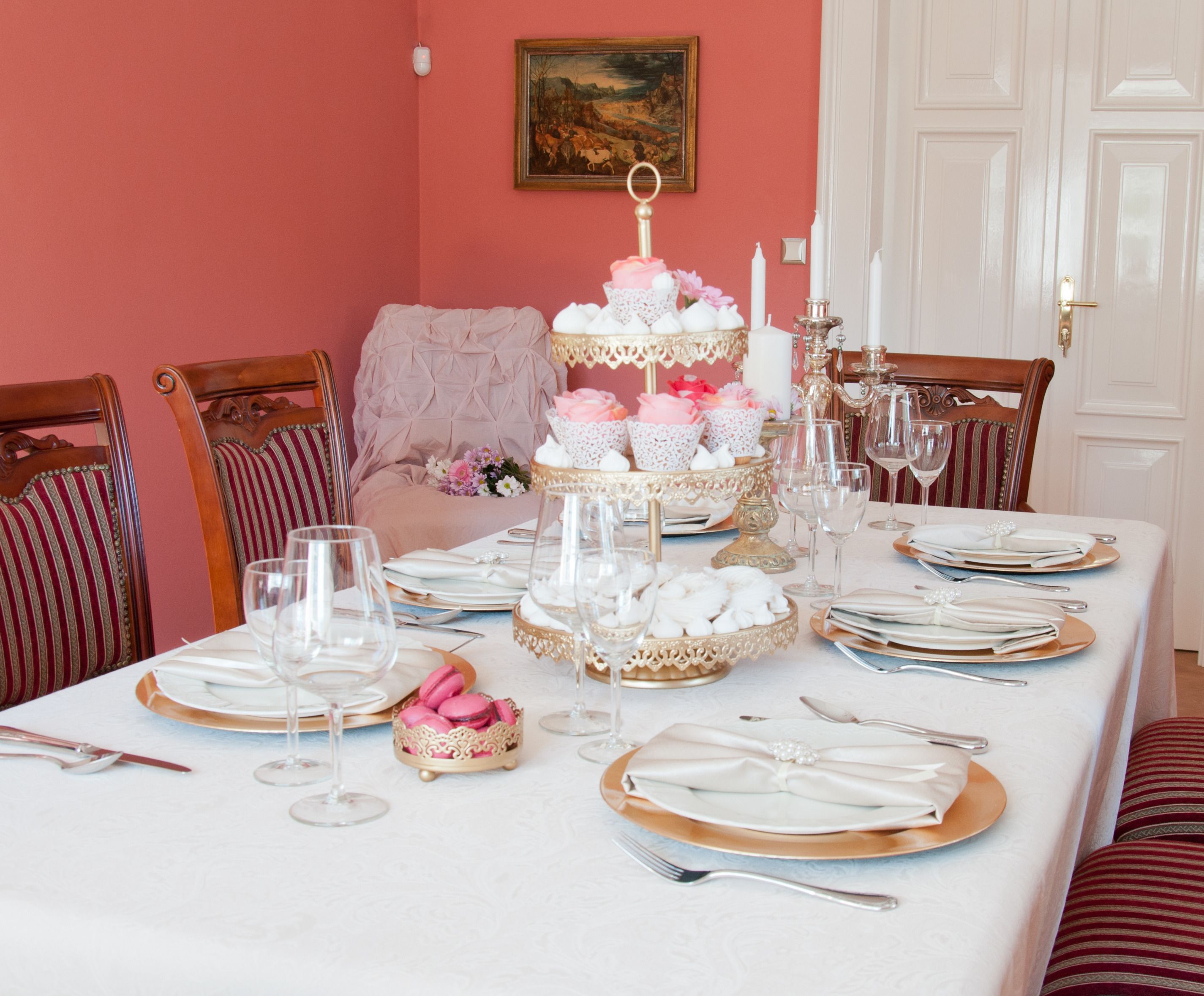 Mesa formal dispuesta con platos blancos y dorados, copas y un soporte escalonado para macarons rosados.