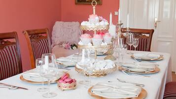 Mesa formal dispuesta con platos blancos y dorados, copas y un soporte escalonado para macarons rosados.