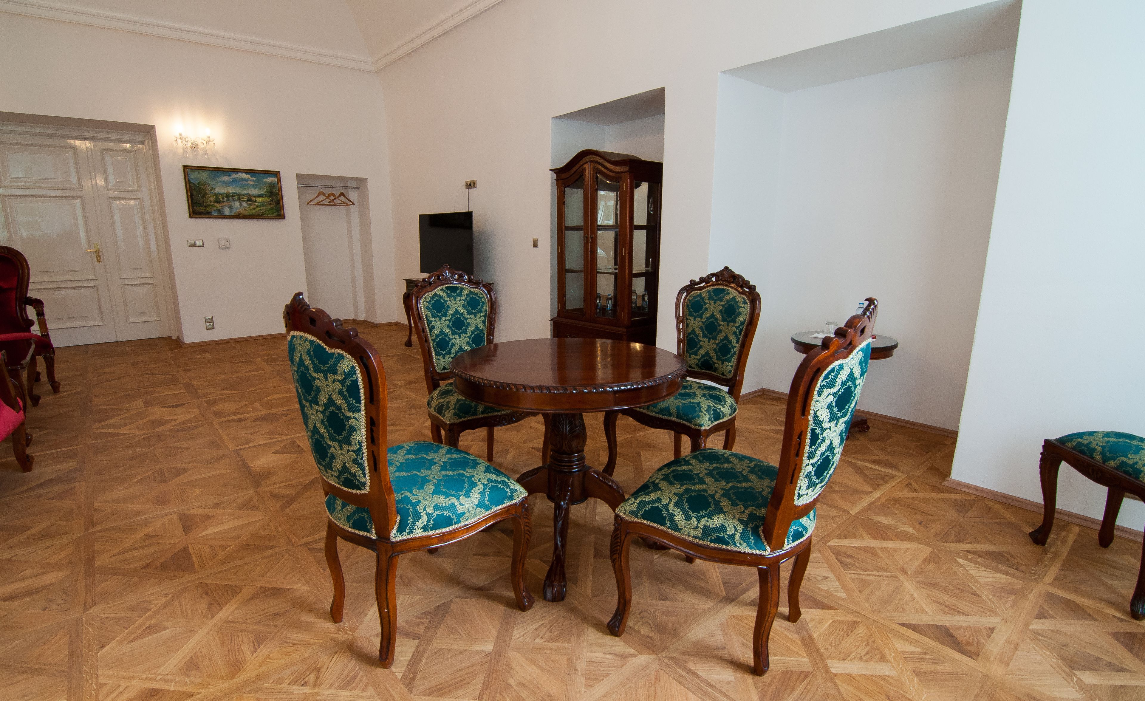 A dining room with a round wooden table surrounded by six chairs with green upholstered seats and backs.