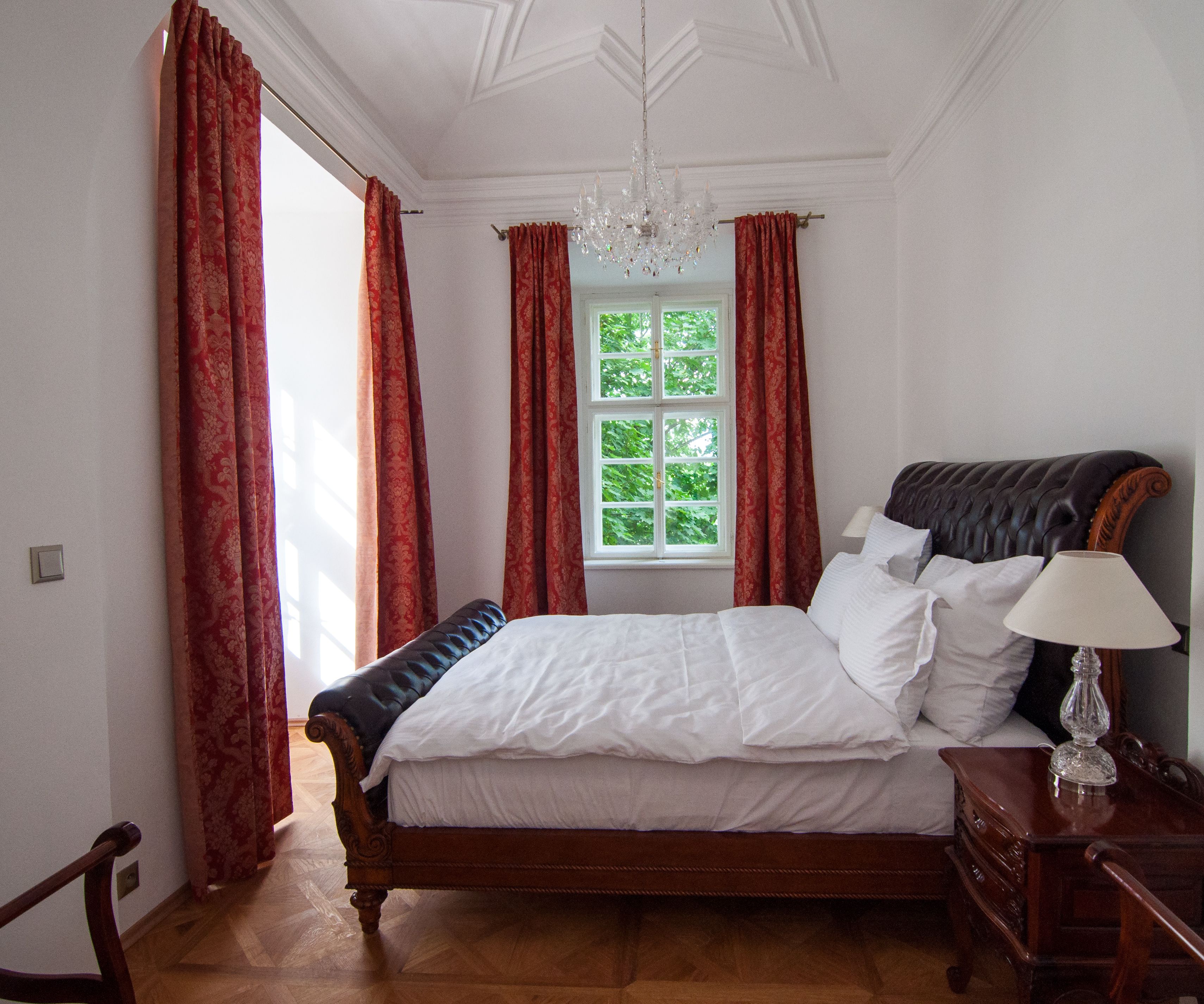 Ein Schlafzimmer mit einem großen Bett, einer Chandelieber und einem Fenster mit Vorhängen.