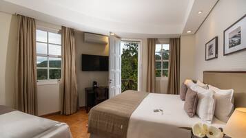 A hotel room with a bed, a desk, a chair, a TV, and a balcony with curtains.