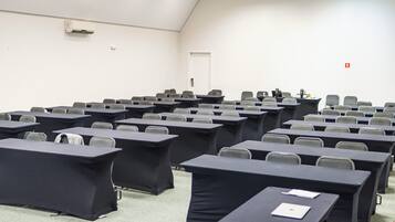 A conference room with rows of tables and chairs, a whiteboard, and an air conditioning unit on the wall.