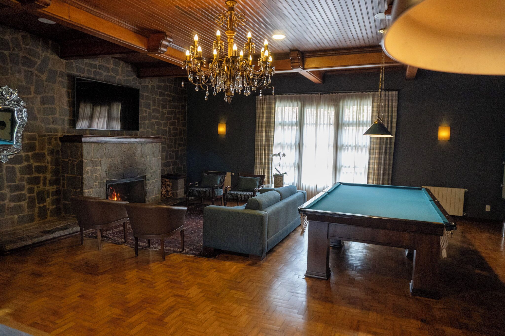 Una habitación acogedora con mesa de billar, asientos cómodos, chimenea y candelabro.