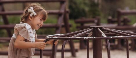 A child playing on a seesaw in a sandy area with wooden structures in the background.
