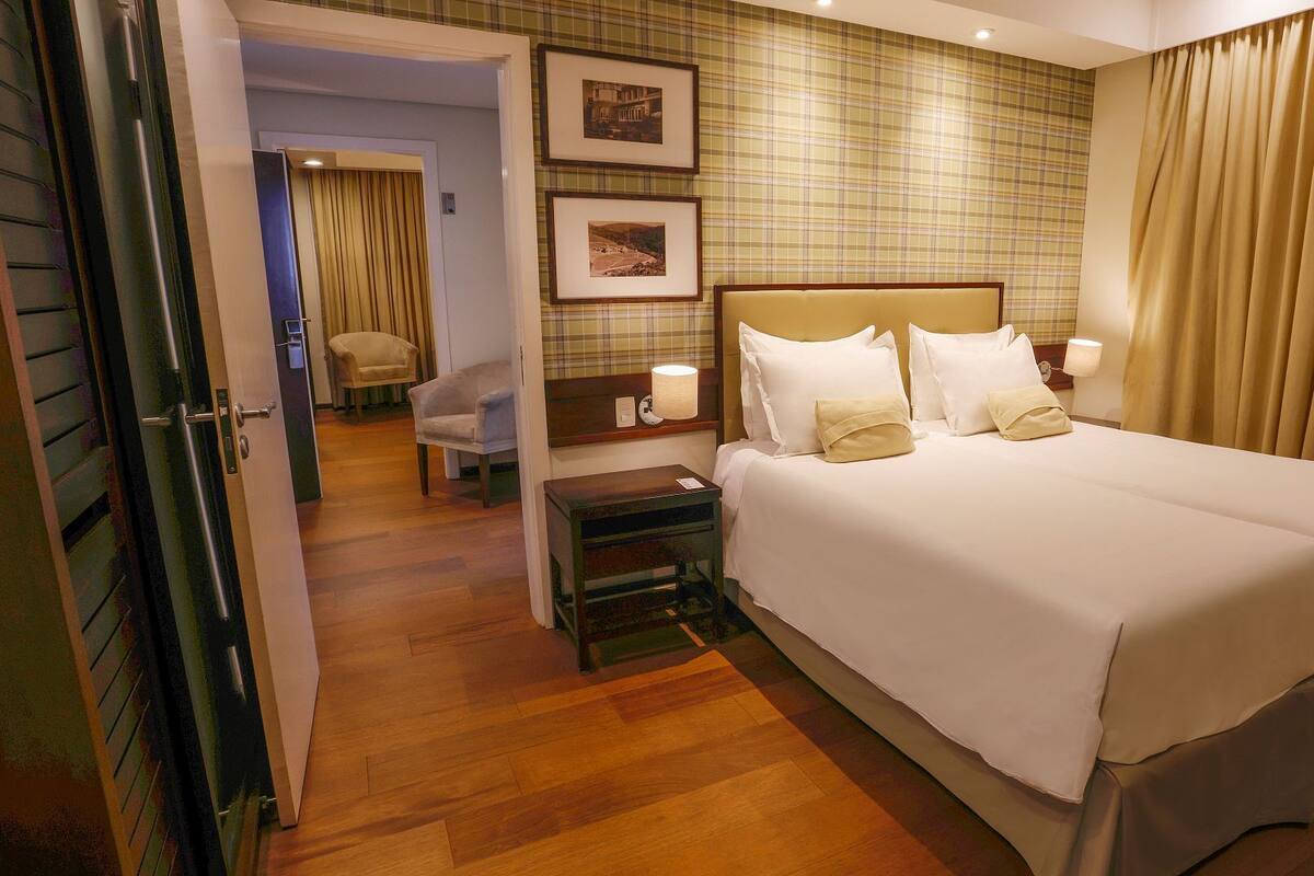 Habitación de hotel con una cama grande, una mesita de noche, una silla y una pared decorada con cuadros.