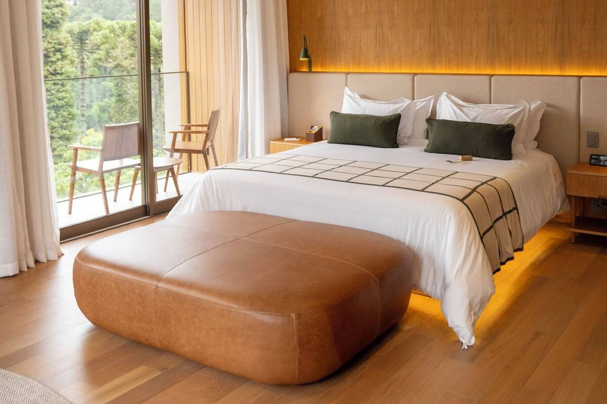 Un dormitorio moderno con una cama grande, cabecera de madera, piso de madera y un balcón con una silla.