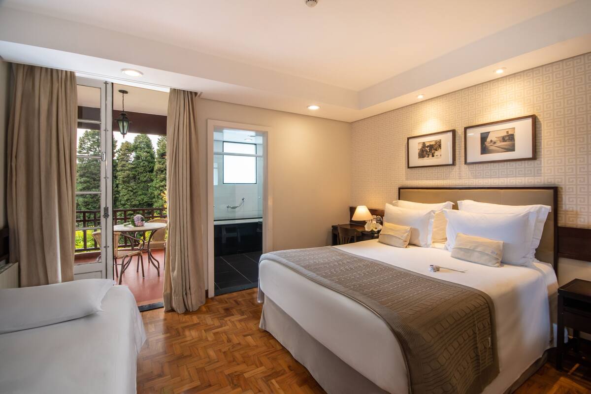 Habitación de hotel con una cama grande, un escritorio, una silla y un balcón con mesa y sillas.