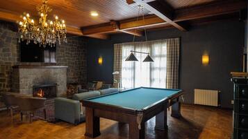 A cozy room with a pool table, comfortable seating, a fireplace, and a chandelier.