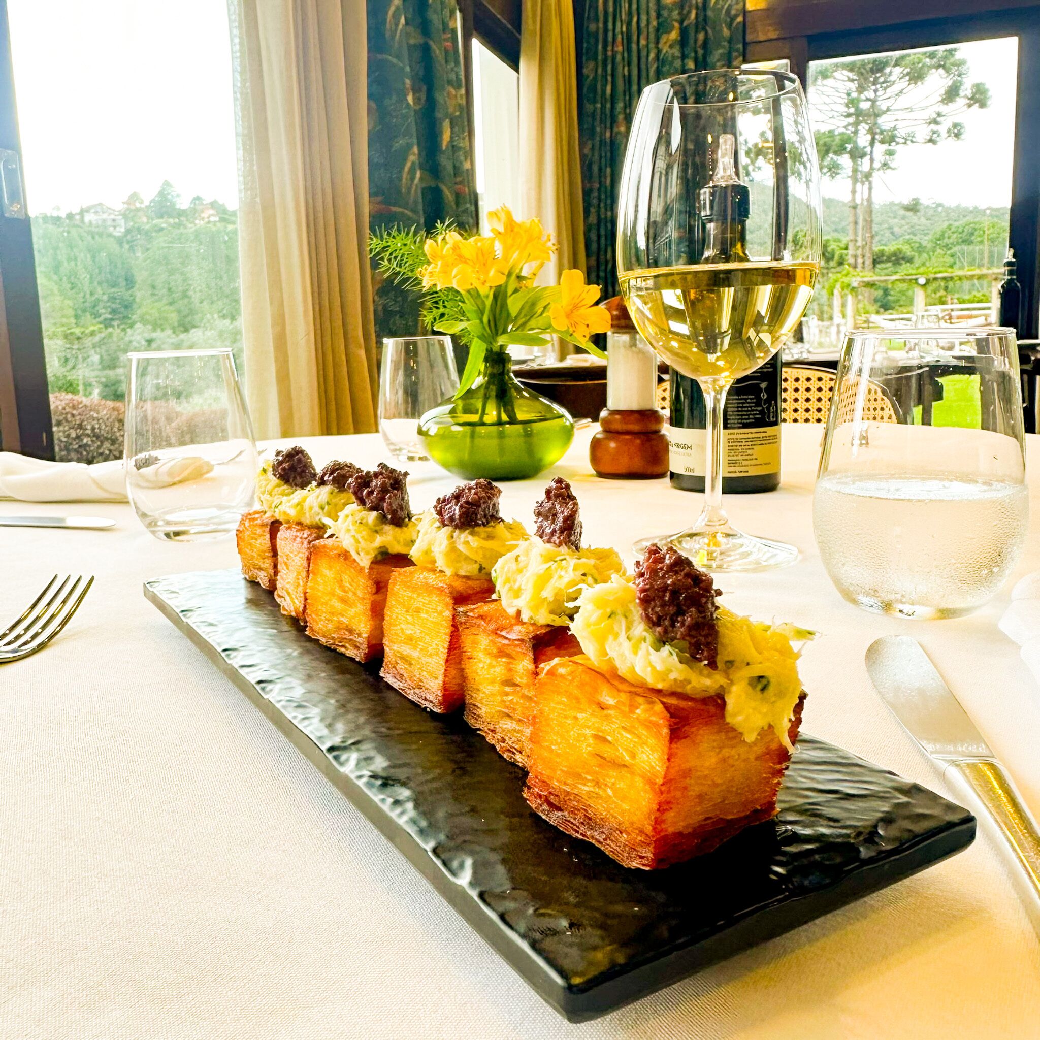 Un postre sobre un plato negro, con una vista panorámica a través de una ventana.