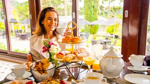 Uma mesa de café da manhã com diversos doces, um bule de chá, xícaras e uma tigela de frutas.