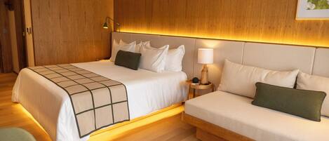 A hotel room with a large bed, a smaller sofa, wooden paneling, a lamp, and a rug.