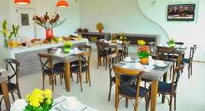 A dining area with multiple tables and chairs, a central island with a vase of flowers, and a television mounted on the wall.