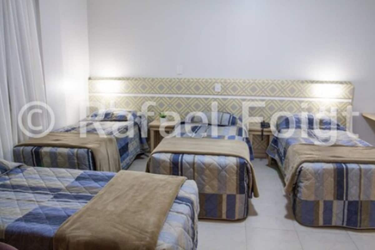 Habitación de hotel con cuatro camas dispuestas en fila, cada una con una colcha estampada.