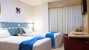 A hotel room with two beds, a desk, a chair, a TV, and a window with curtains. - BR Suítes Hotel (Navegantes)