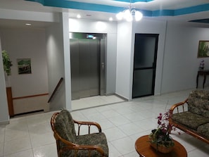 A lobby with two elevators, a staircase, and seating area with a plant on a table.