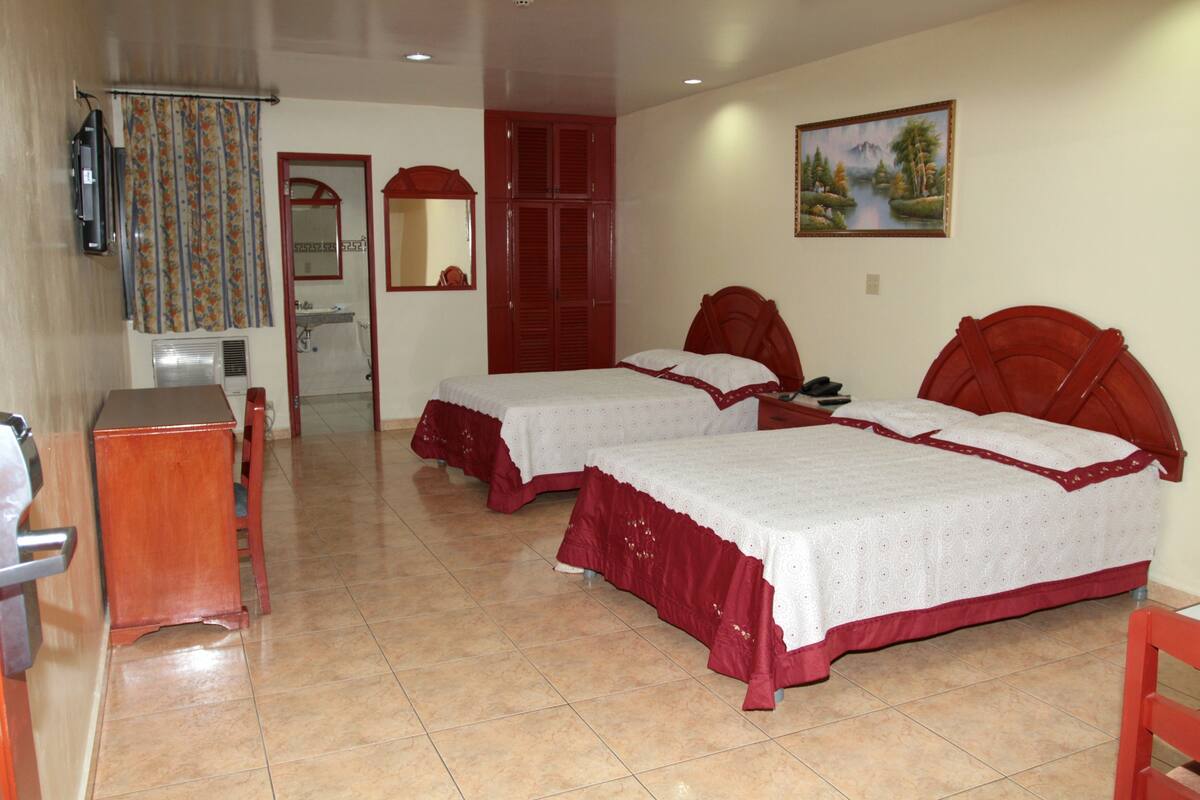 A hotel room with two beds, a bathroom, a TV, and a painting on the wall.