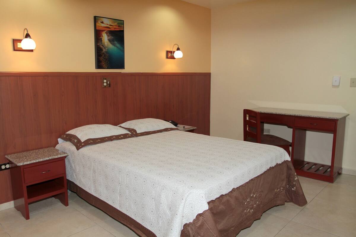 A bedroom with a bed, bedside tables, a desk, and two wall-mounted lamps.