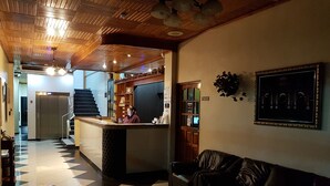 A hotel lobby with a check-in counter, a reception desk, a staircase, and a leather sofa. - Hotel Alcala (David)
