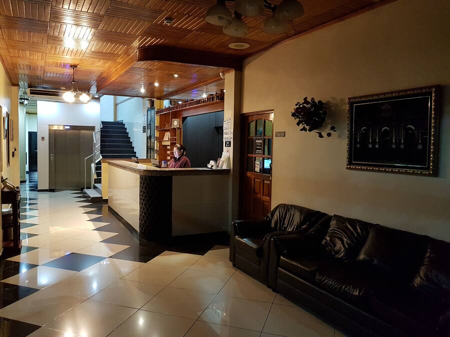 Um hall de hotel com balcão de check-in, mesa de recepção, escada e sofá de couro.