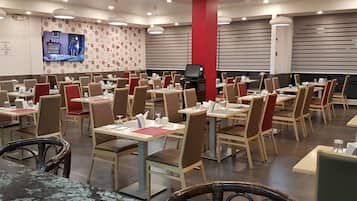 A restaurant with multiple tables and chairs, a television mounted on the wall, and a red pillar.