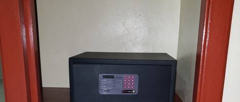 Una caja fuerte negra con teclado digital sobre un estante de madera frente a una pared lisa.