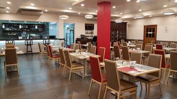 A restaurant with multiple tables and chairs, a bar area, and a kitchen in the background.