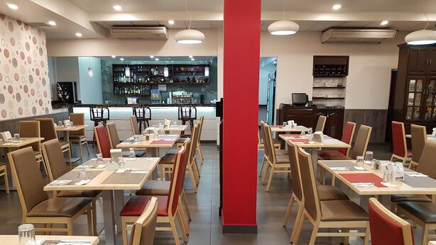 A restaurant with multiple tables and chairs, a bar area, and shelves with bottles and glasses. - Hotel Alcala (David)