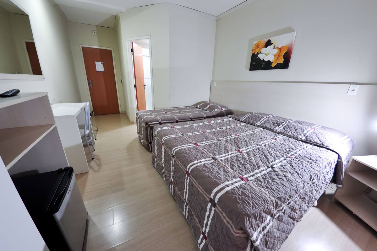 Habitación de hotel con una cama grande, un escritorio, una silla, un armario y un baño visible a través de una puerta abierta.