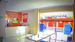 A reception area with a glass partition, a reception desk, and a colorful mural depicting a building. - Klein Ville INN (Esteio)
