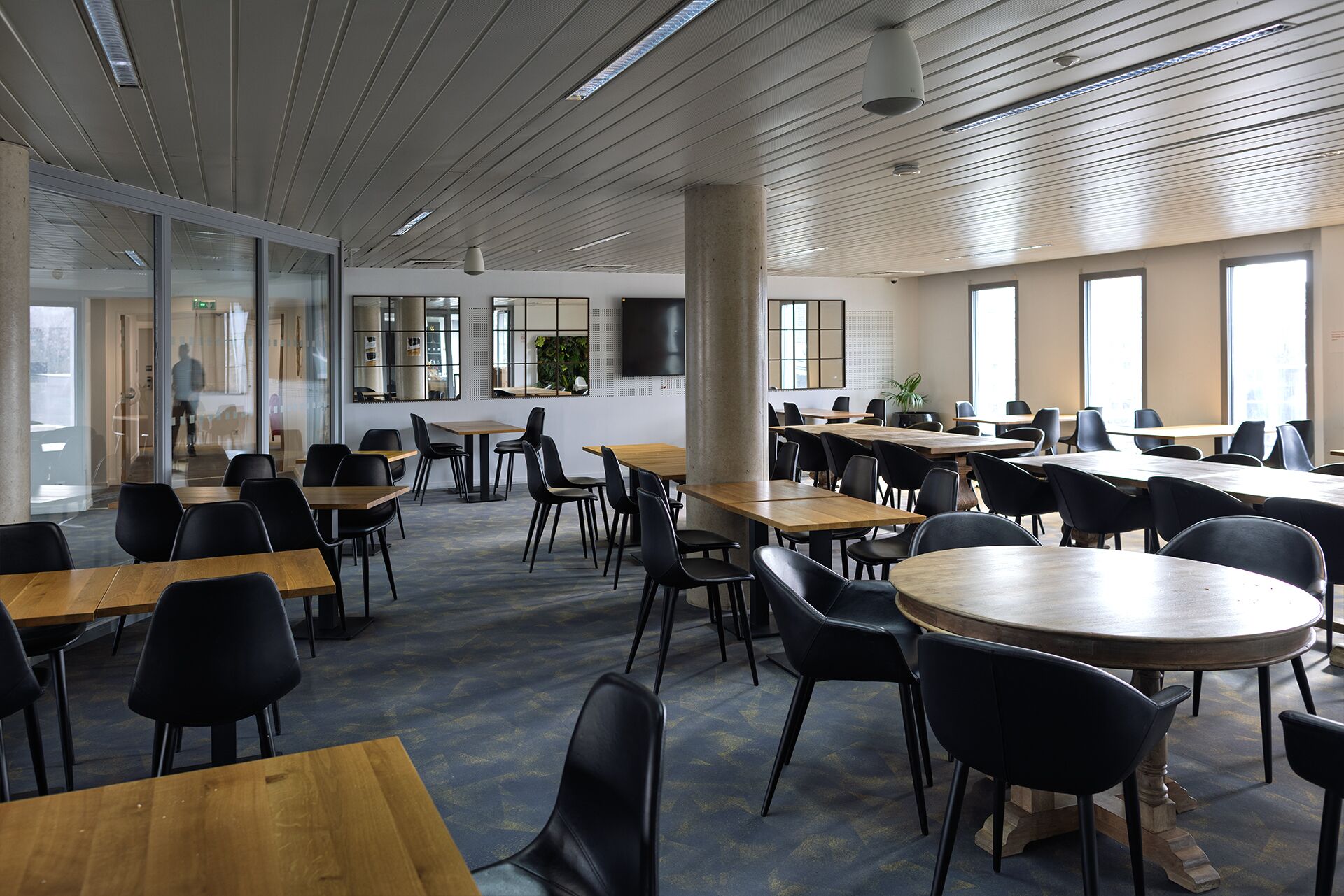 Une salle de conférence spacieuse, dotée de nombreuses tables et chaises, de grandes fenêtres et d’un design de plafond moderne.