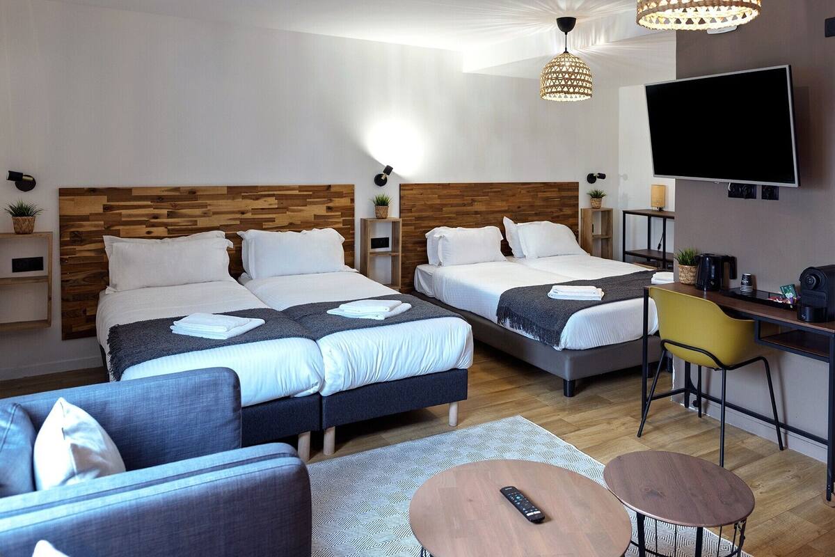 A hotel room with two beds, a sofa, a desk with a chair, a TV, and a coffee maker.