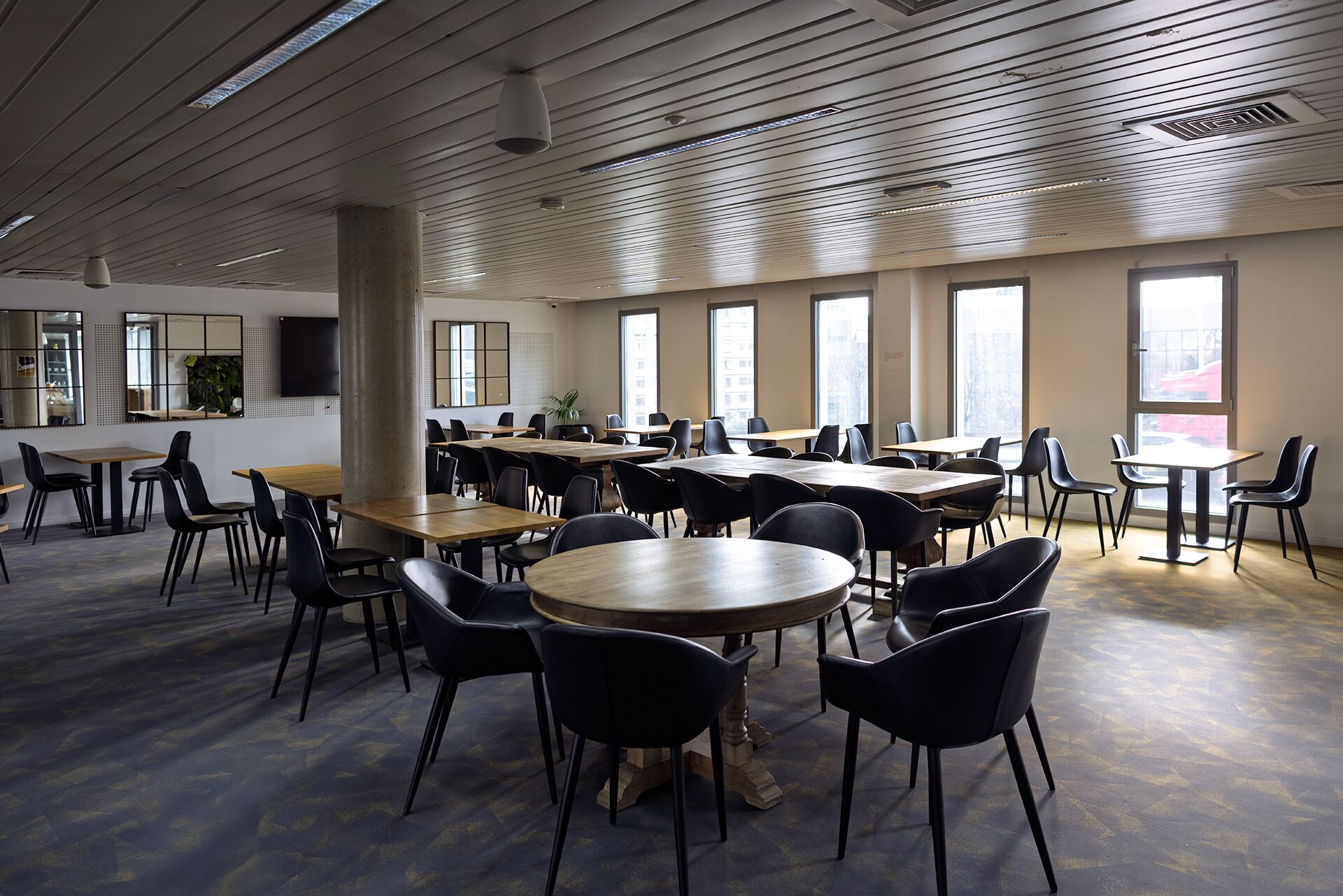 A spacious conference room with multiple tables and chairs, large windows, and a modern ceiling design.