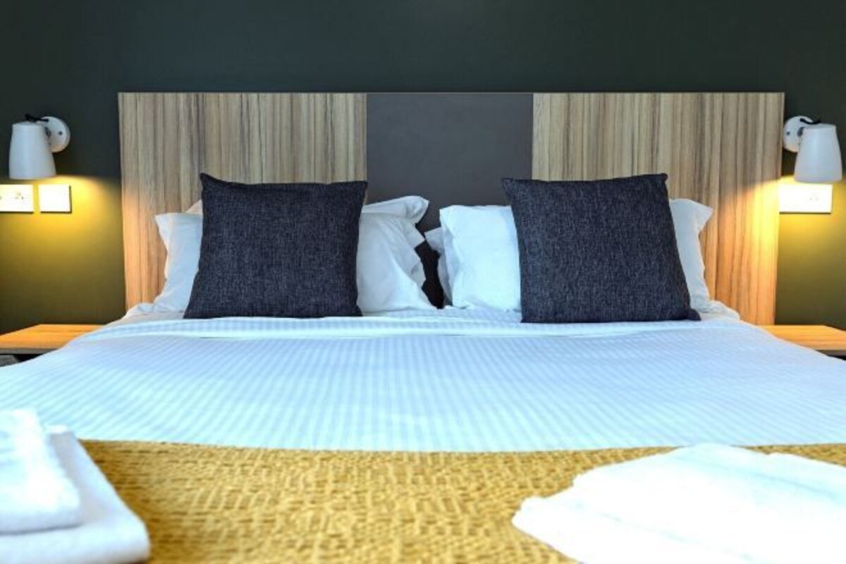 Una cama bien hecha con una colcha a rayas blancas y grises, dos almohadas gris oscuro y una manta color beige.