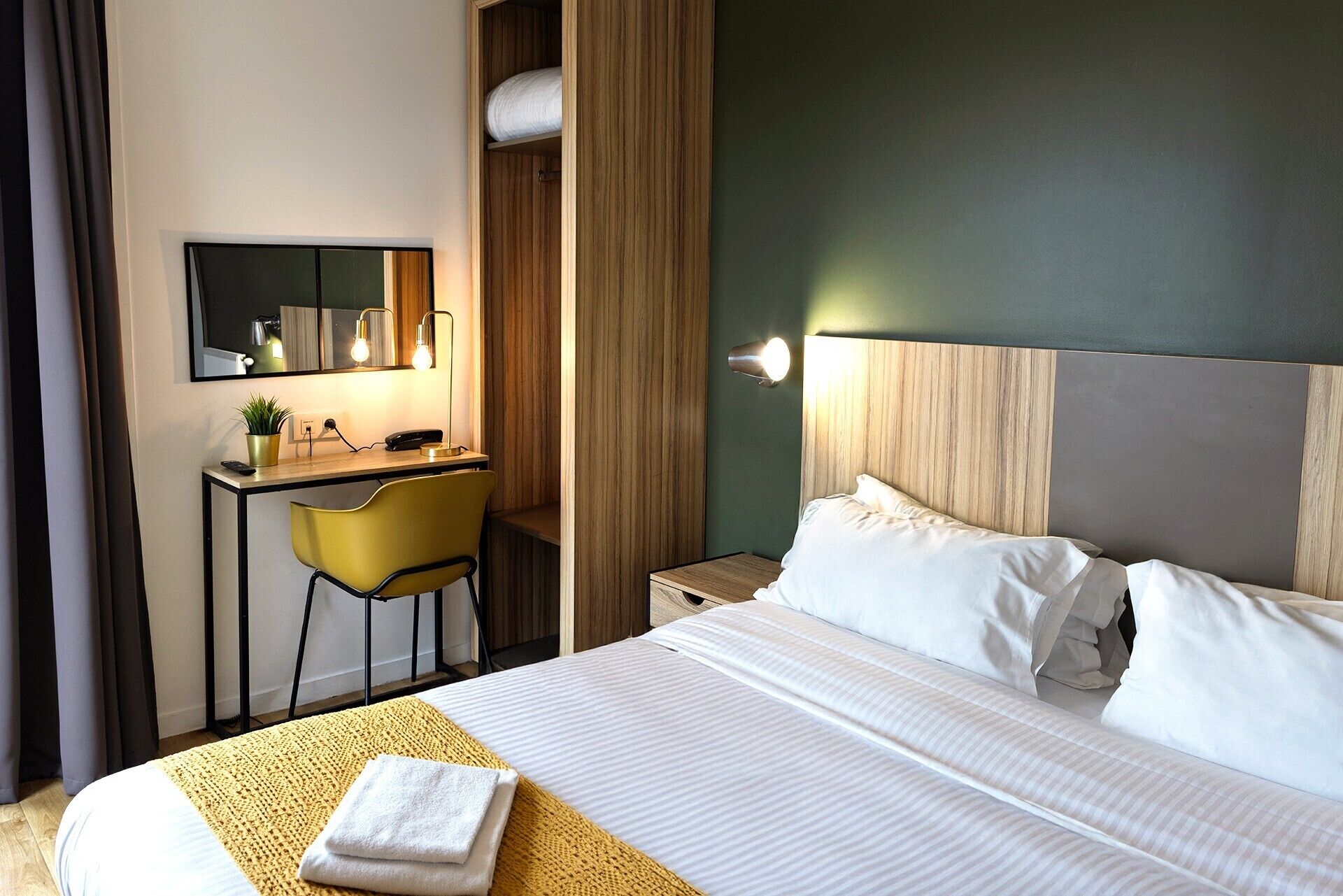 Una habitación de hotel con cama, escritorio, silla, espejo y mesita de noche.