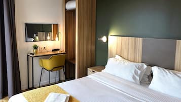 Una habitación de hotel con cama, escritorio, silla, espejo y mesita de noche.