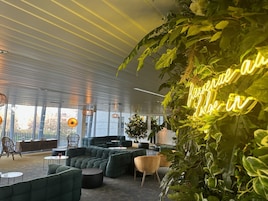 A modern lounge area with green sofas, a neon sign, and large windows.