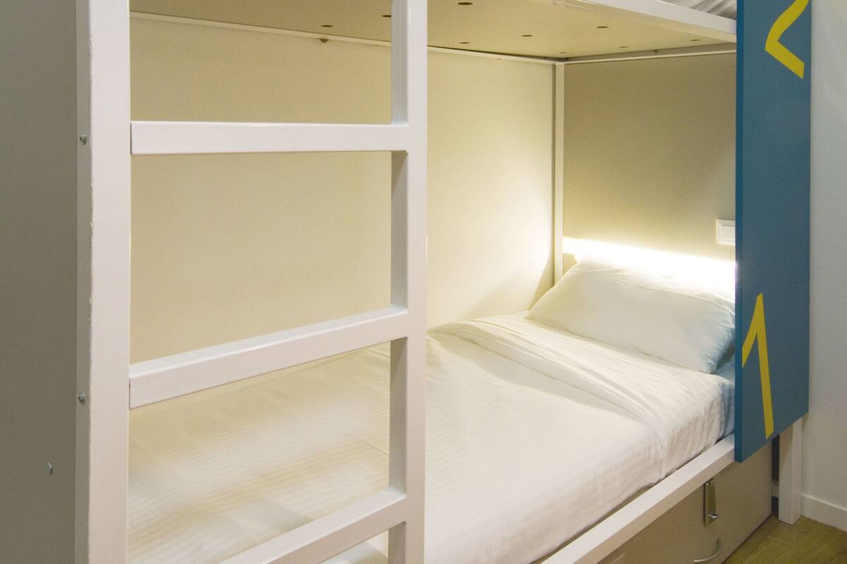 A bunk bed with two levels, each with a mattress and pillows. There is a blue sign with numbers on the wall next to the bed.