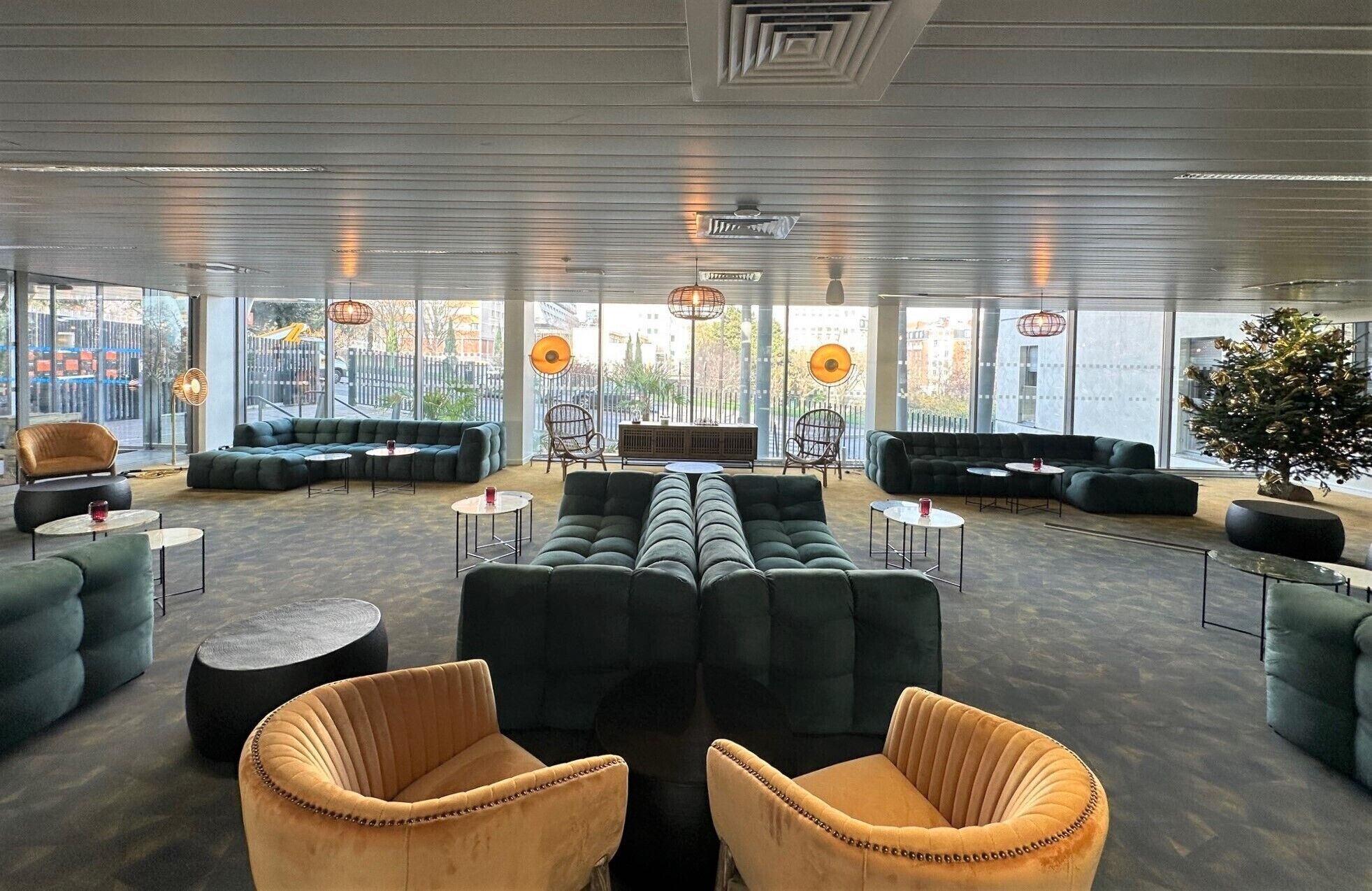 A spacious lounge area with multiple seating options including sofas and chairs, large windows offering views of the city, and a modern ceiling design.