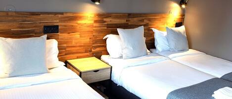 A hotel room with two beds, wooden headboard, bedside tables, and wall-mounted lights.