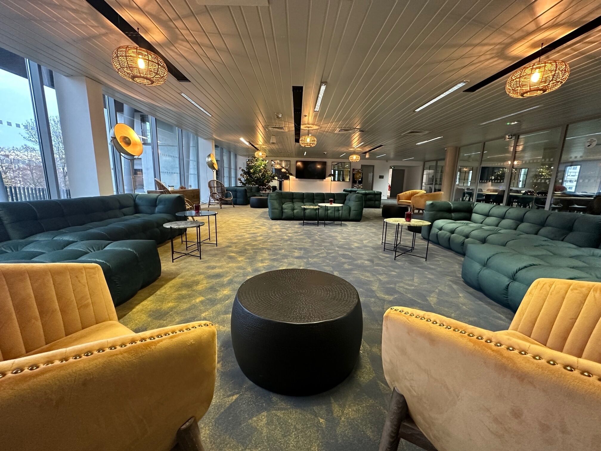 Een ruime zithoek met groene banken, gele fauteuils en een zwart hocker in het midden.