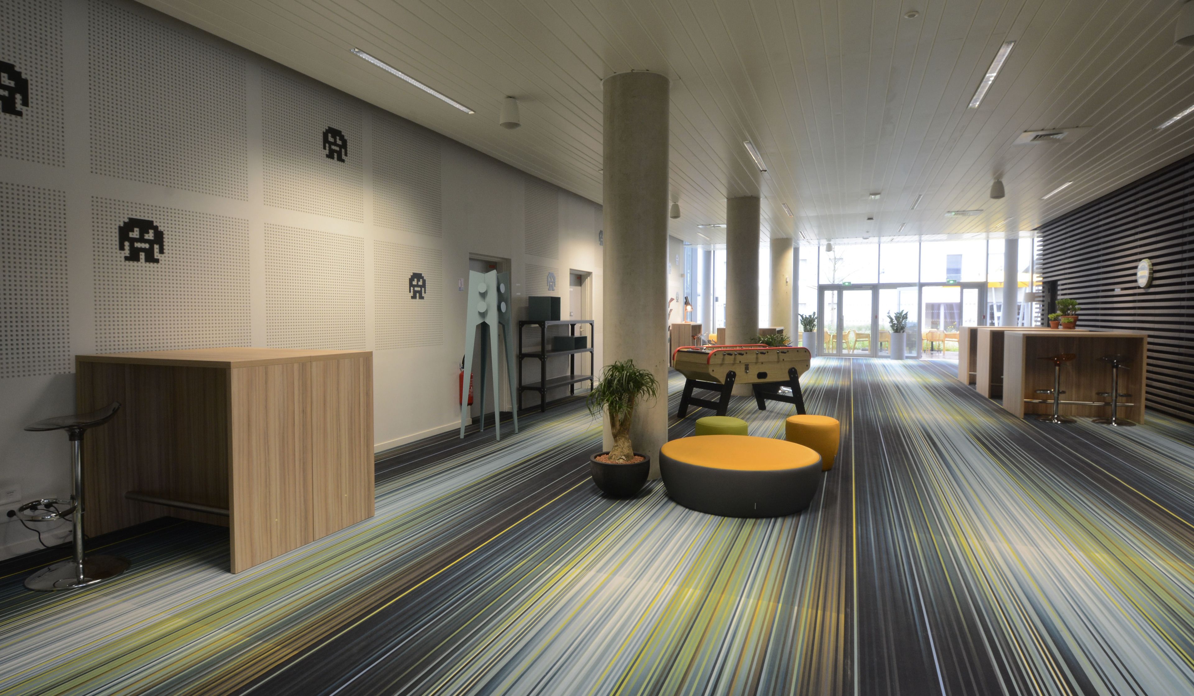 Een moderne lobby met een gestreept tapijt, een houten receptiebalie, een zithoek en een groot raam dat voor natuurlijk licht zorgt.