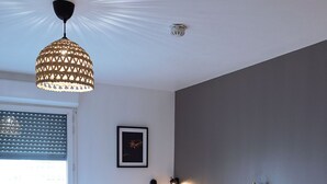 A hotel room with two beds, a wooden headboard, a large window with blinds, a hanging light fixture, and a framed picture on the wall.